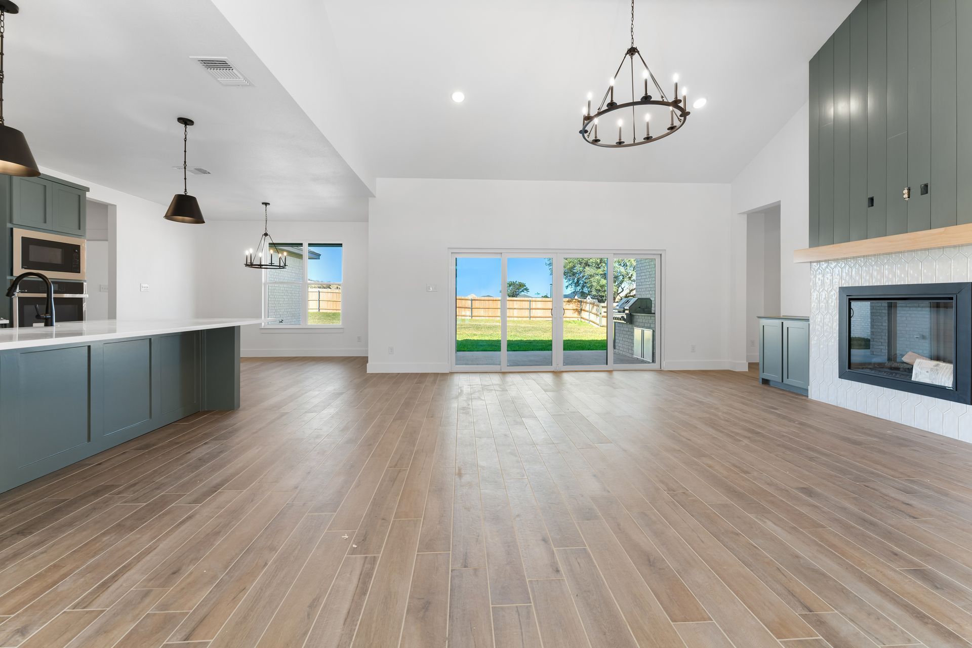 Spacious modern living space with wooden floors, kitchen, and fireplace. Large windows look out to a yard.