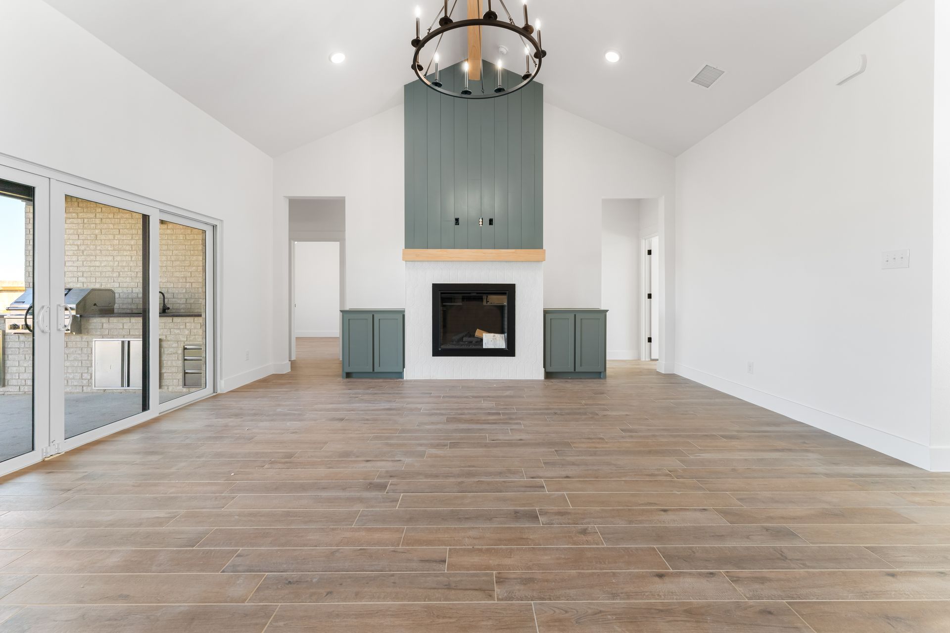 Empty room with fireplace, built-in cabinets, and sliding glass door. Wood-look flooring, white walls, and blue-green cabinets.