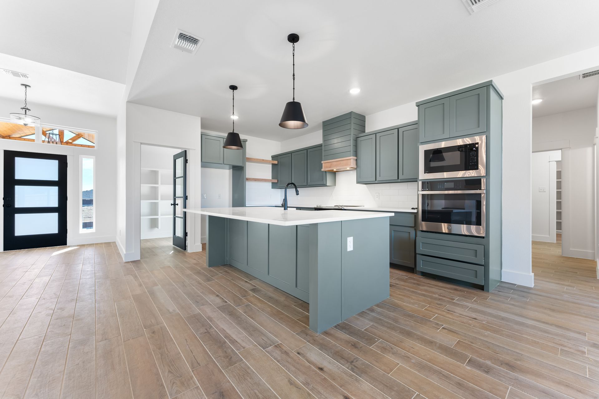 Modern kitchen with teal cabinets, large island, and wood floors. Black pendant lights.