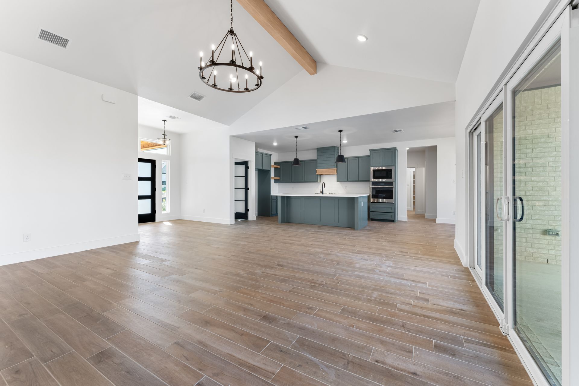 Spacious interior with wood floors, vaulted ceiling, open kitchen, and sliding glass door.