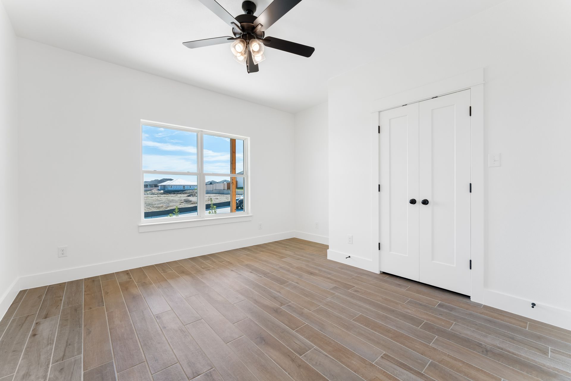 Empty bedroom with hardwood floors, white walls, and a large window.