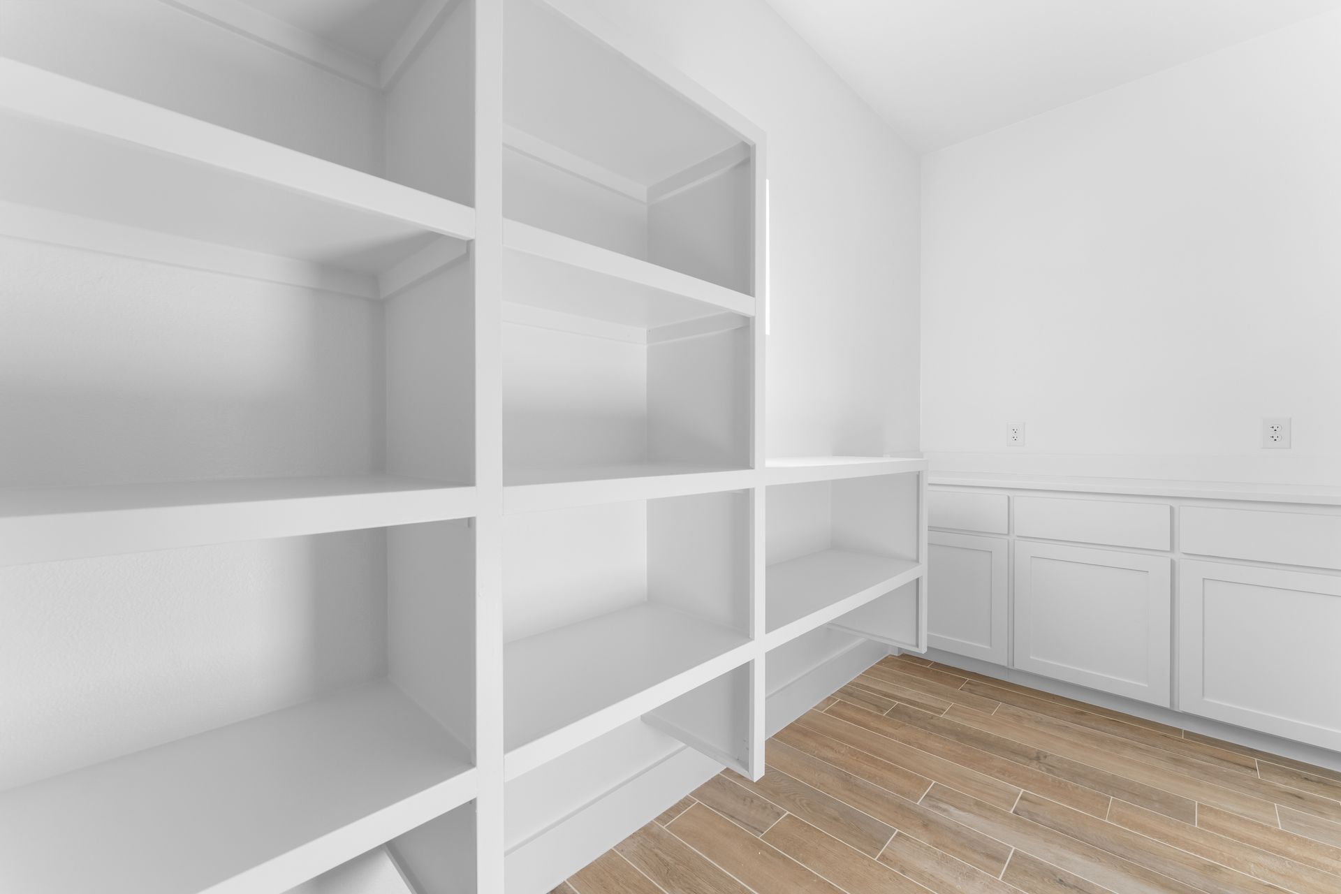 White shelving unit with multiple shelves, adjacent to white cabinets.