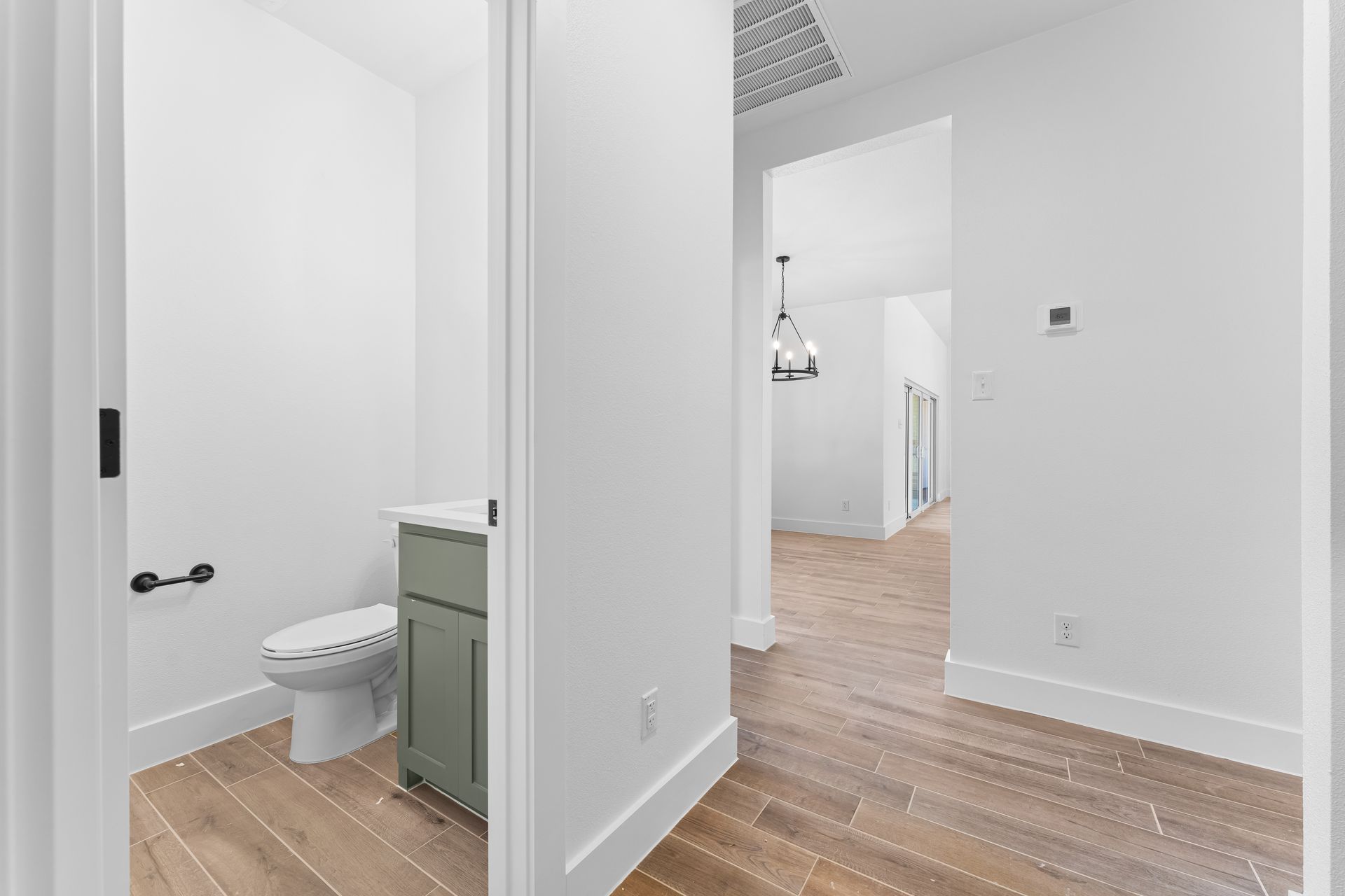 White hallway with a bathroom on the left, light wood floors, and neutral walls.