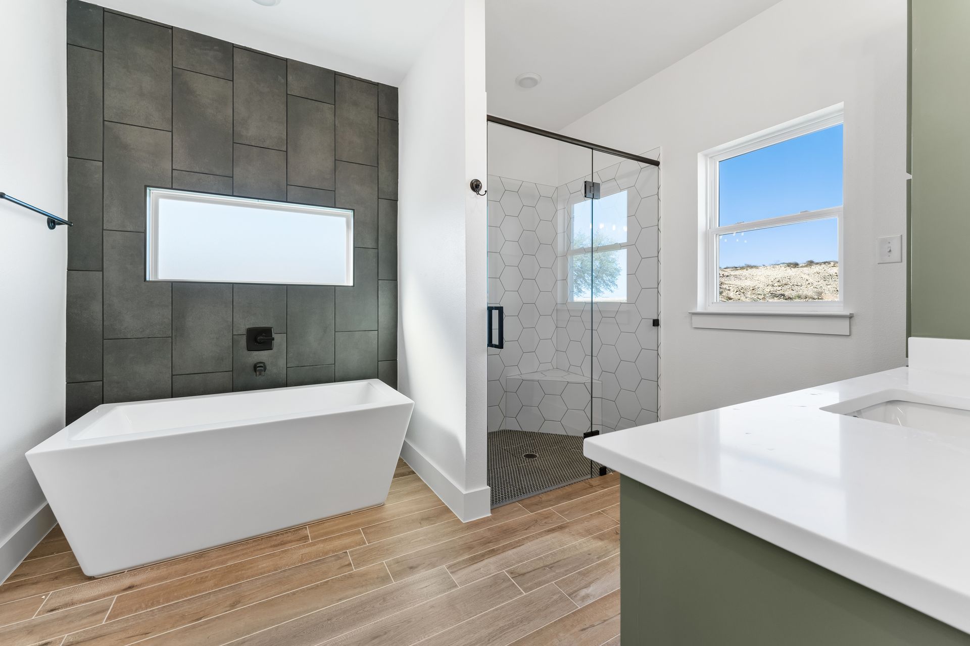 Modern bathroom with a bathtub, shower, and white countertop. Dark gray accent wall, and light wood flooring.