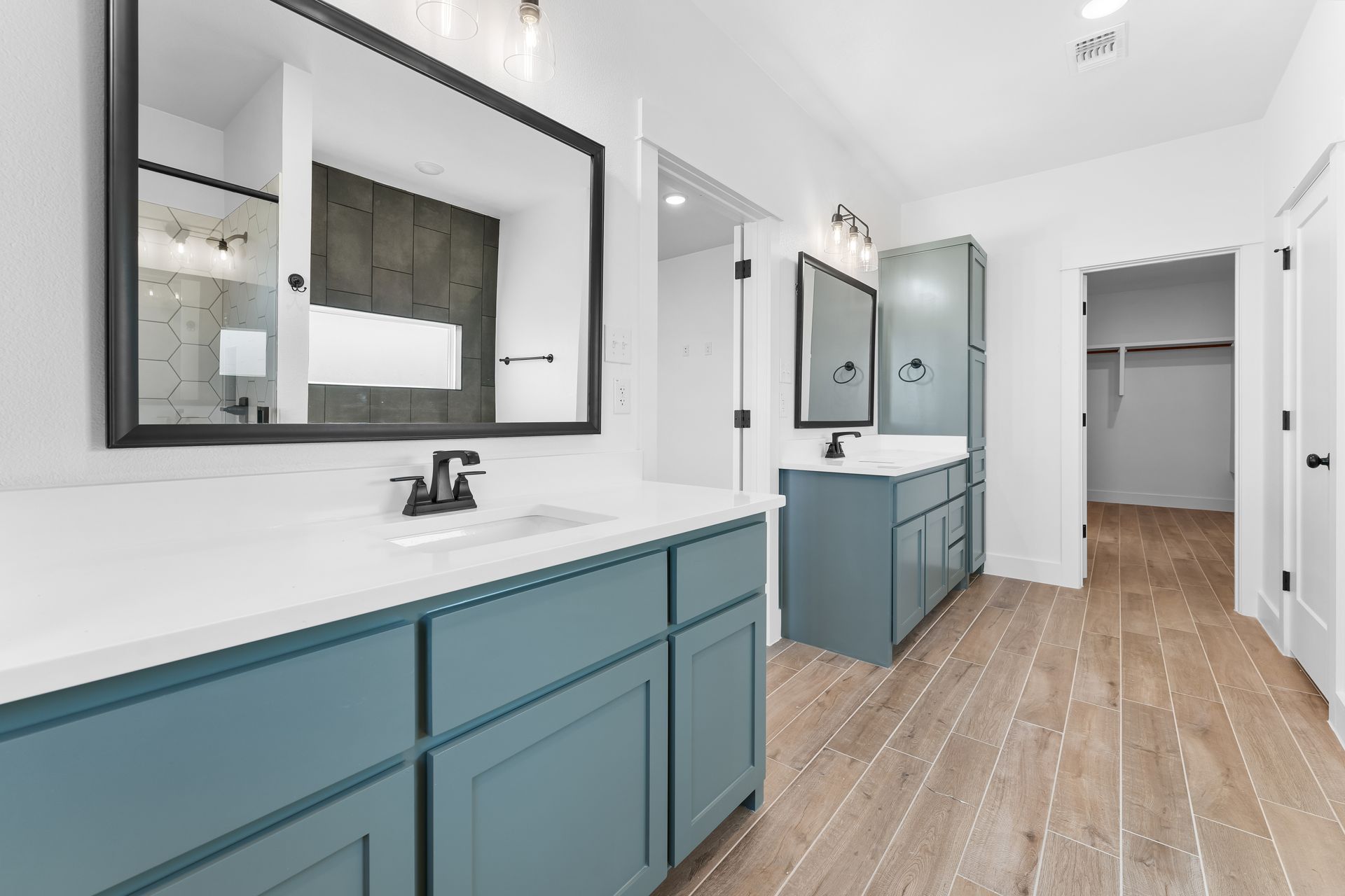 Bathroom with teal vanities, white countertops, large mirrors, and wood-look flooring.