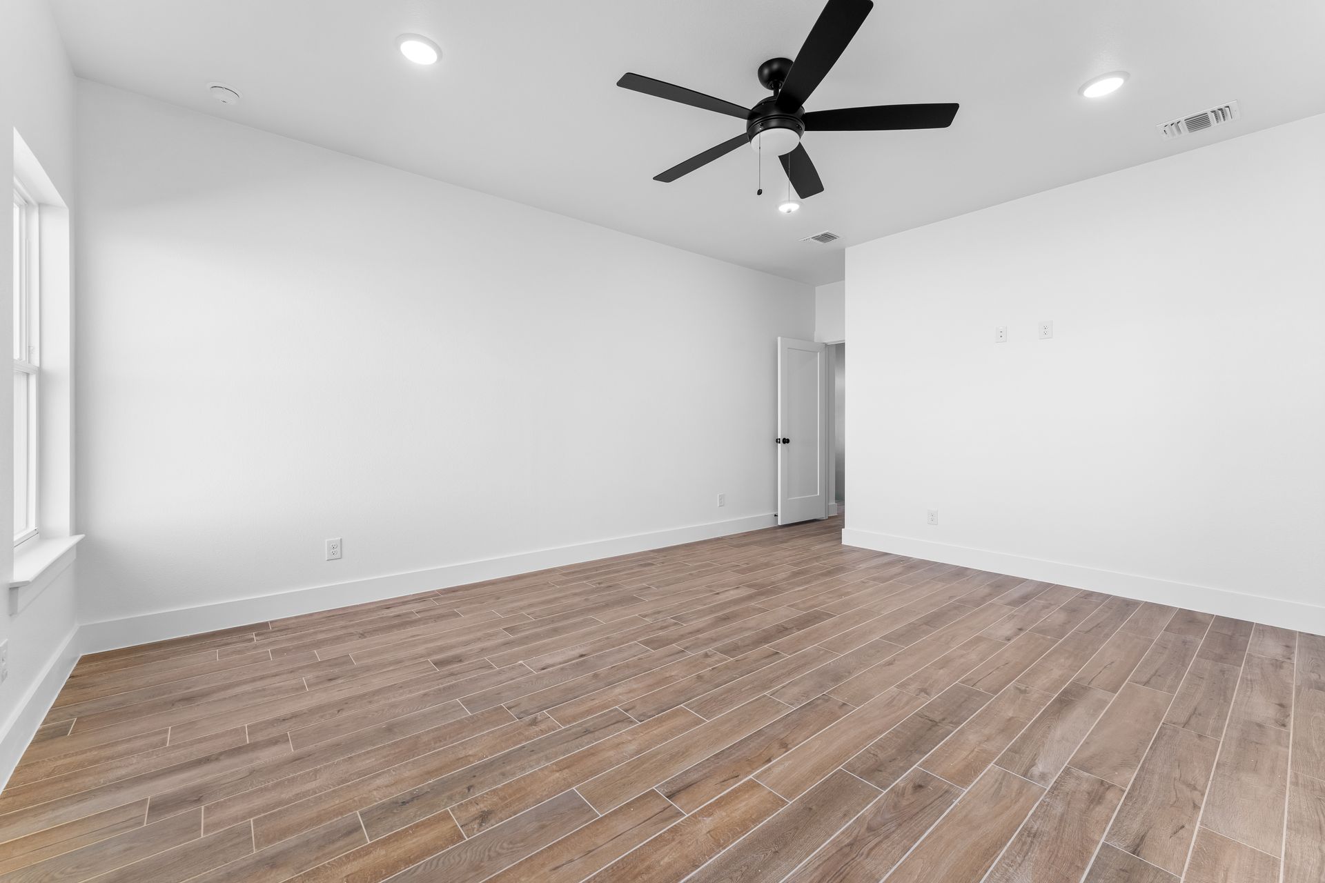 Empty room with hardwood floors, white walls, ceiling fan, and recessed lighting.