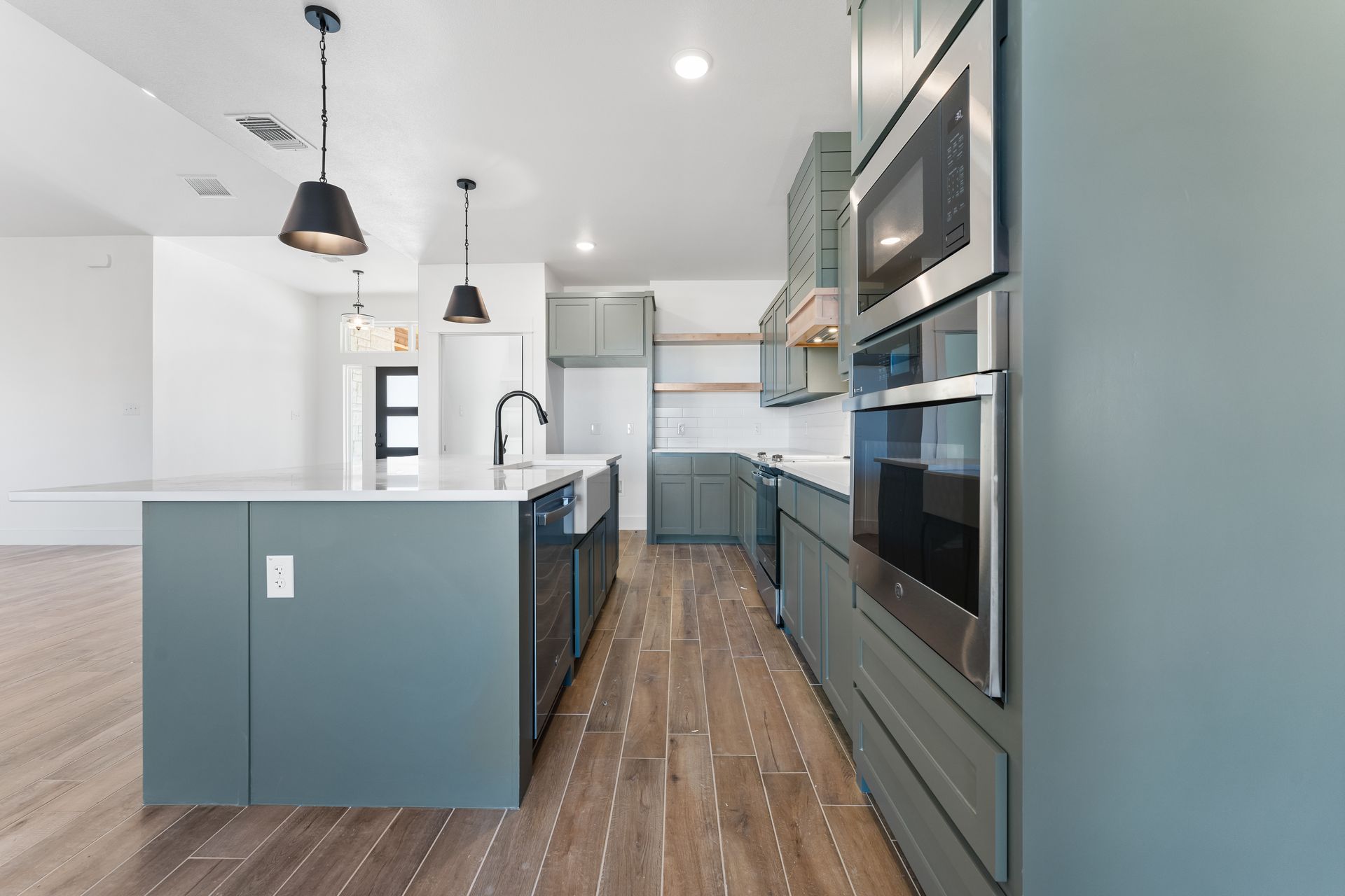 Modern kitchen with teal cabinets, stainless steel appliances, and wood floors.