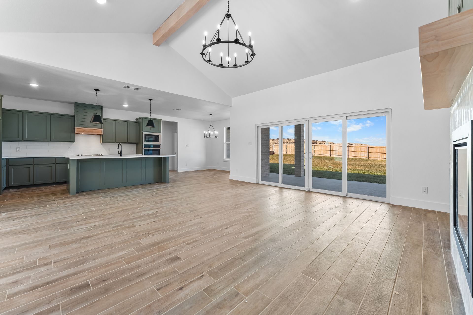 Open-concept kitchen and living area with sage green cabinets, light wood floors, and large sliding glass doors.