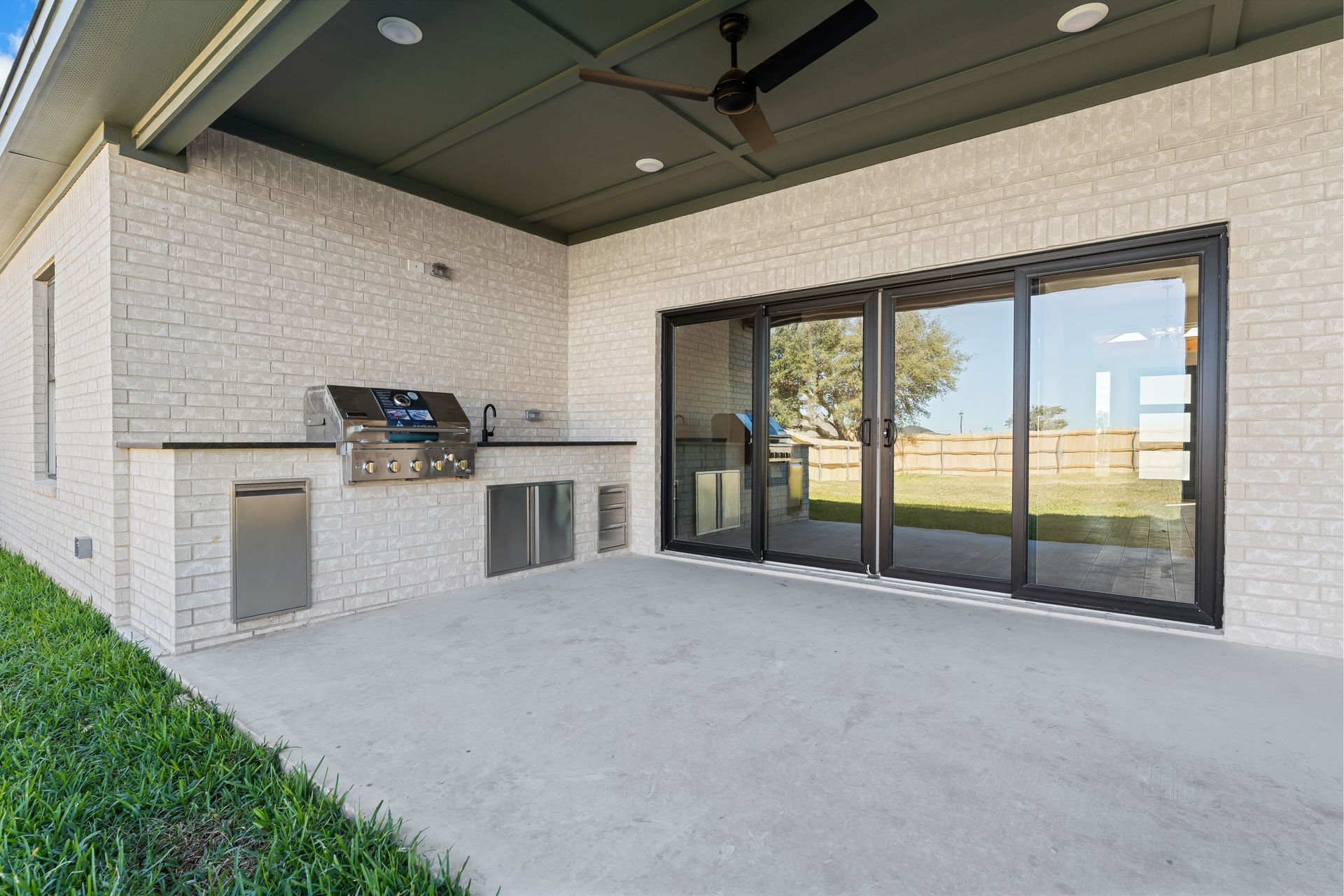 Outdoor patio with built-in grill, large glass doors, and light brick walls.
