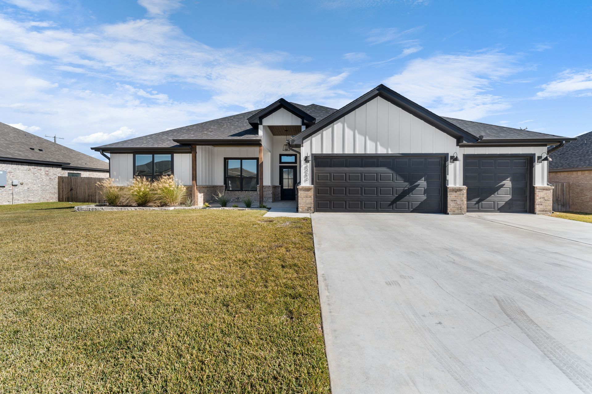 Modern white house with dark garage doors, long driveway, and lawn.
