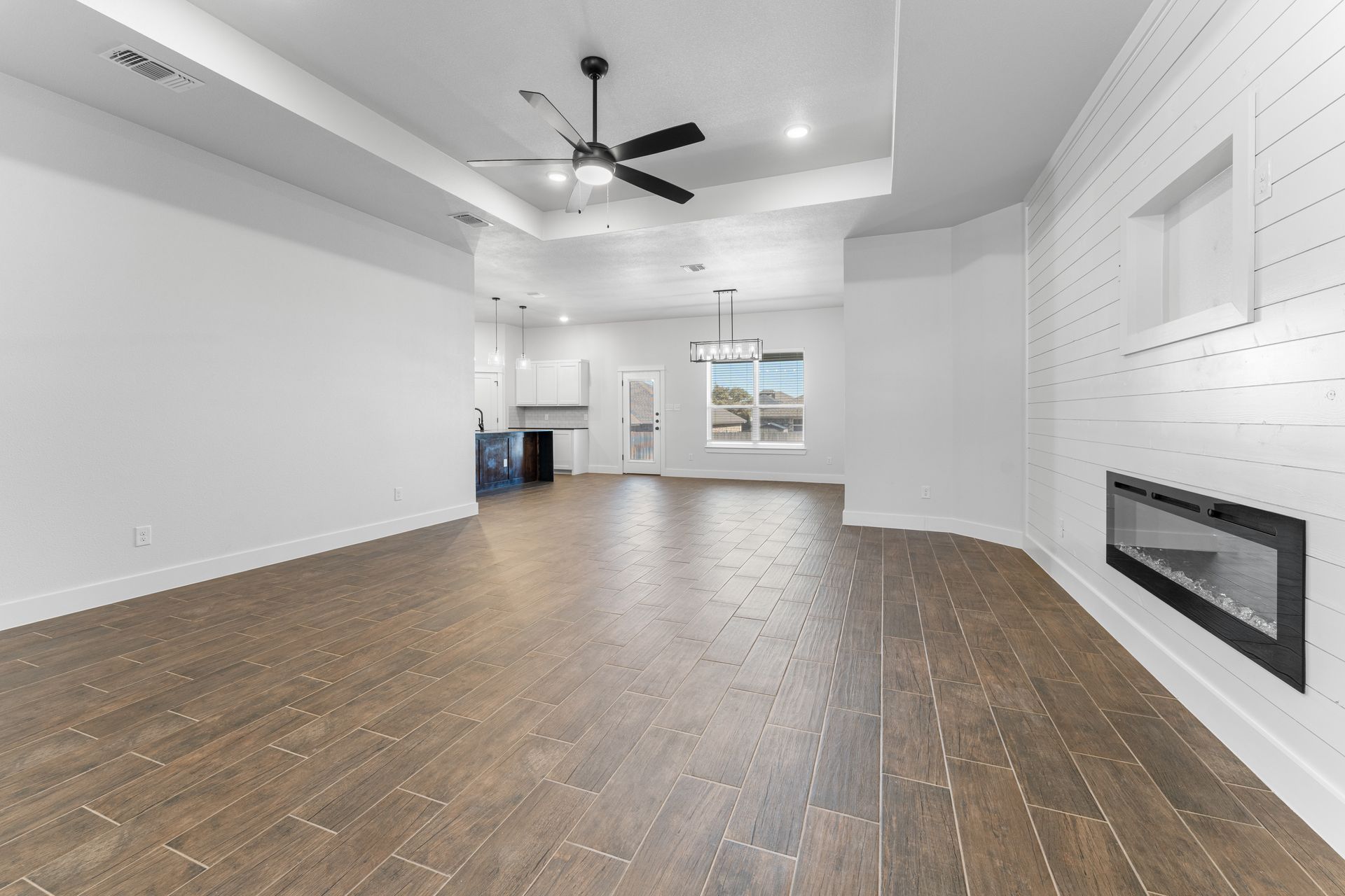 Empty modern living room with wood floors, white walls, and fireplace.