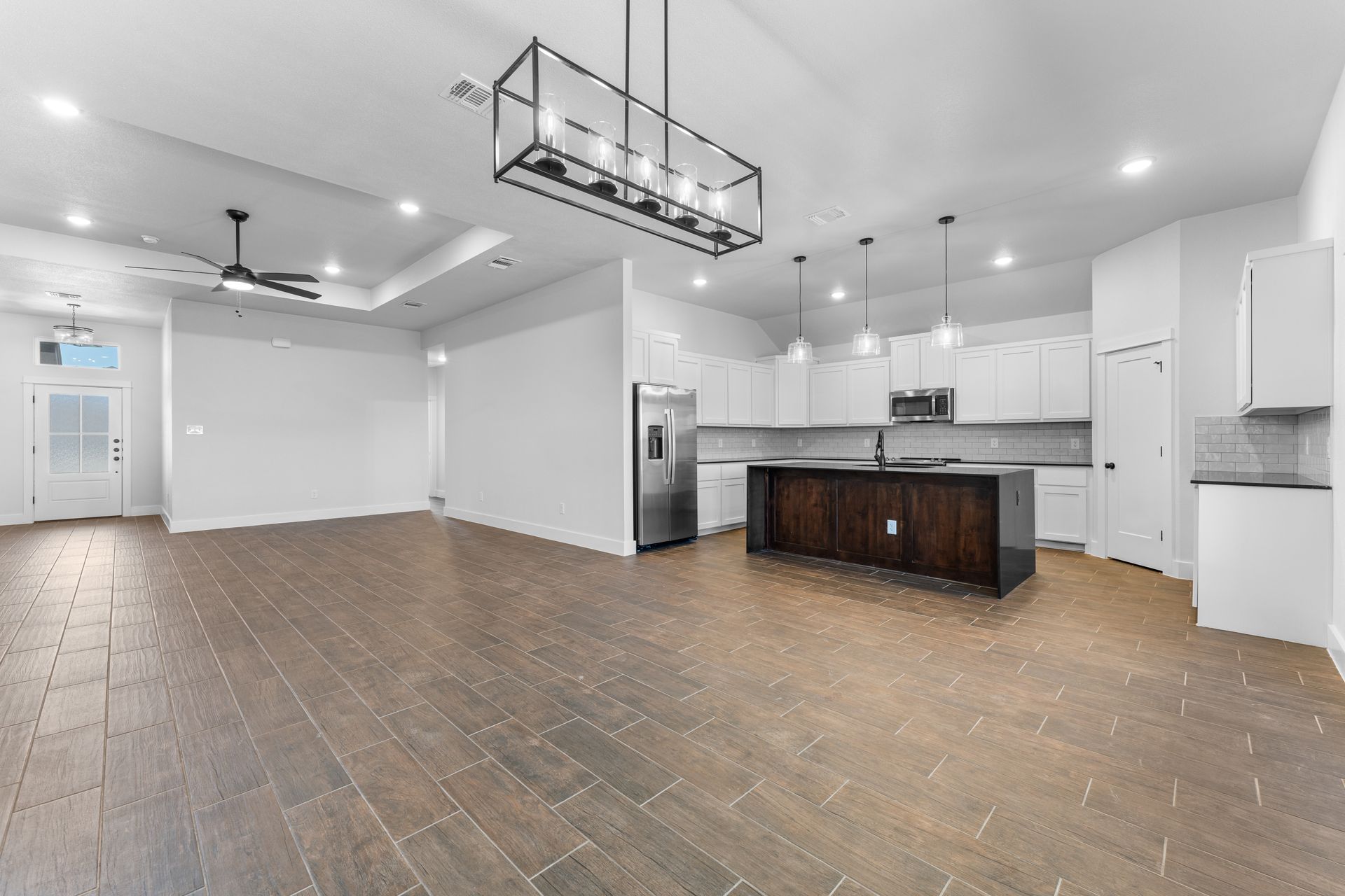Open-concept living space with dark wood floors and a modern kitchen featuring a dark island and white cabinetry.