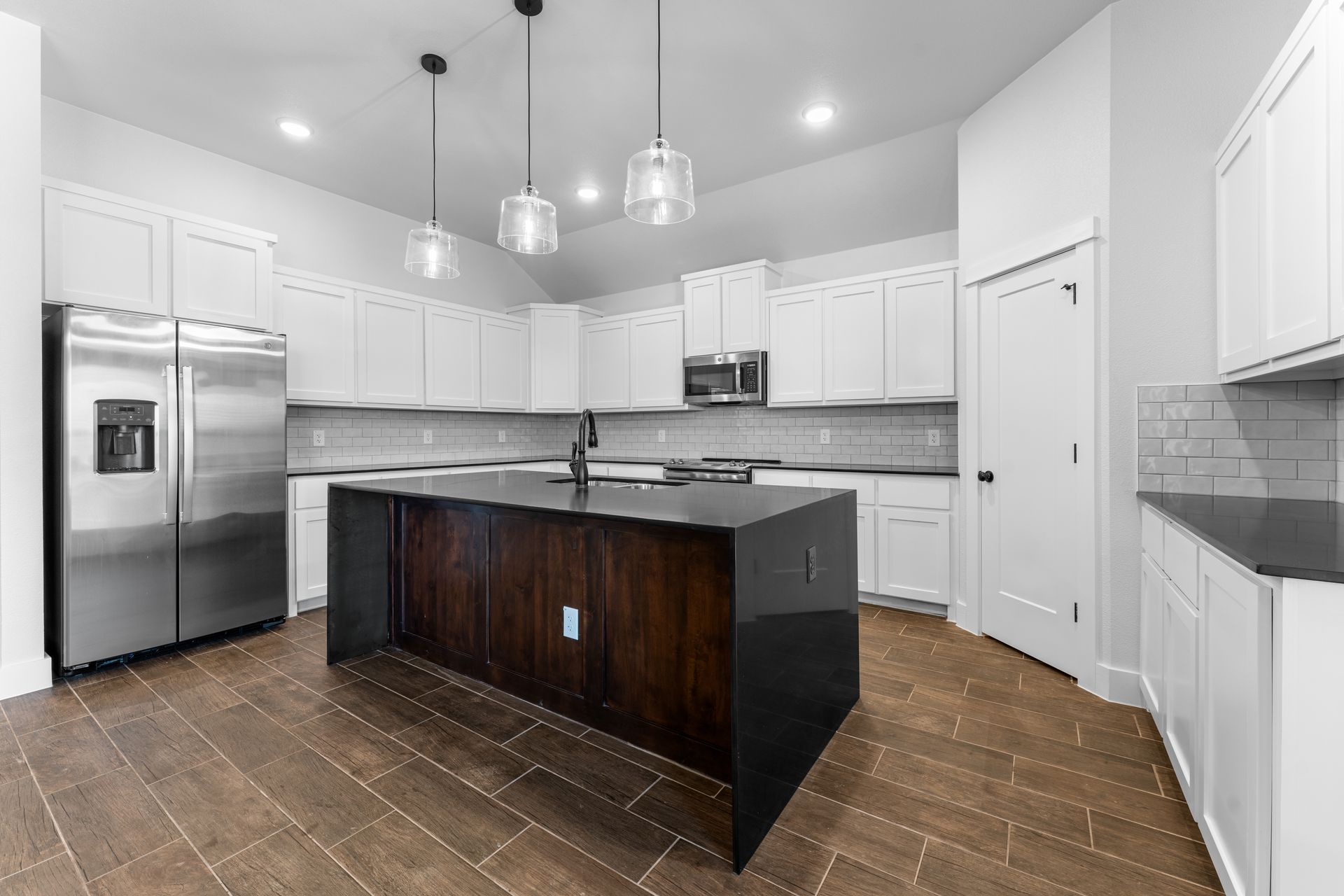 Modern kitchen with white cabinets, dark island, and stainless steel appliances.