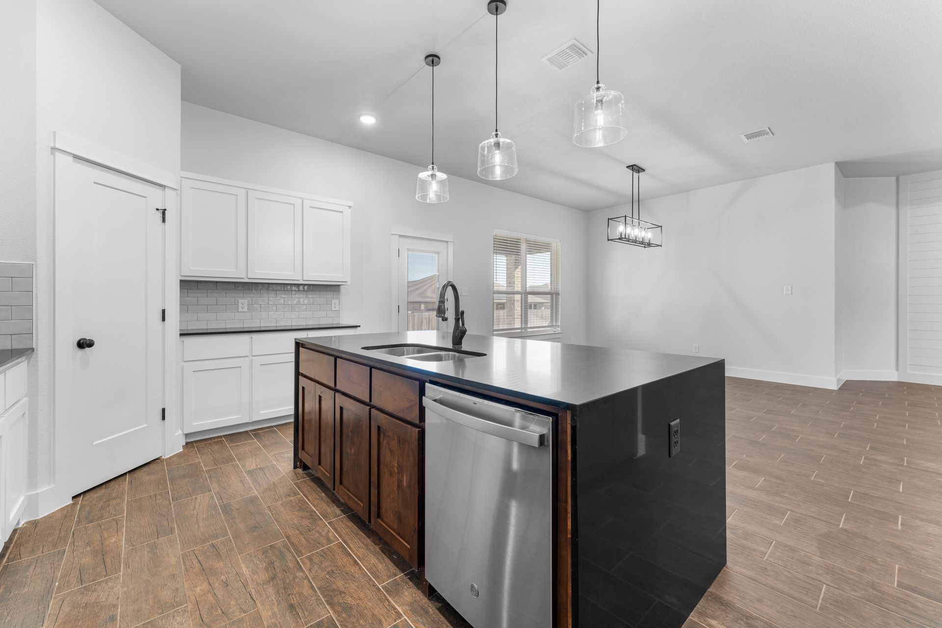 Modern kitchen with island, stainless steel appliances, and white cabinets. Brown wooden flooring.