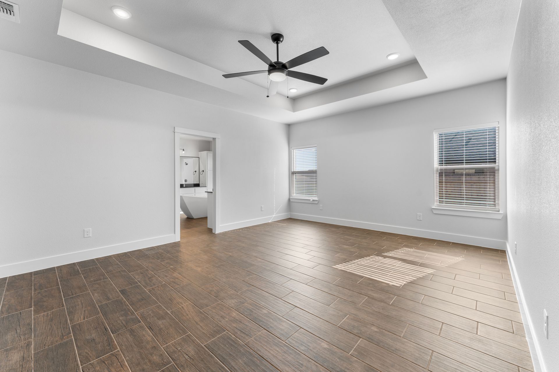 Empty bedroom with hardwood floors, white walls, and a ceiling fan.