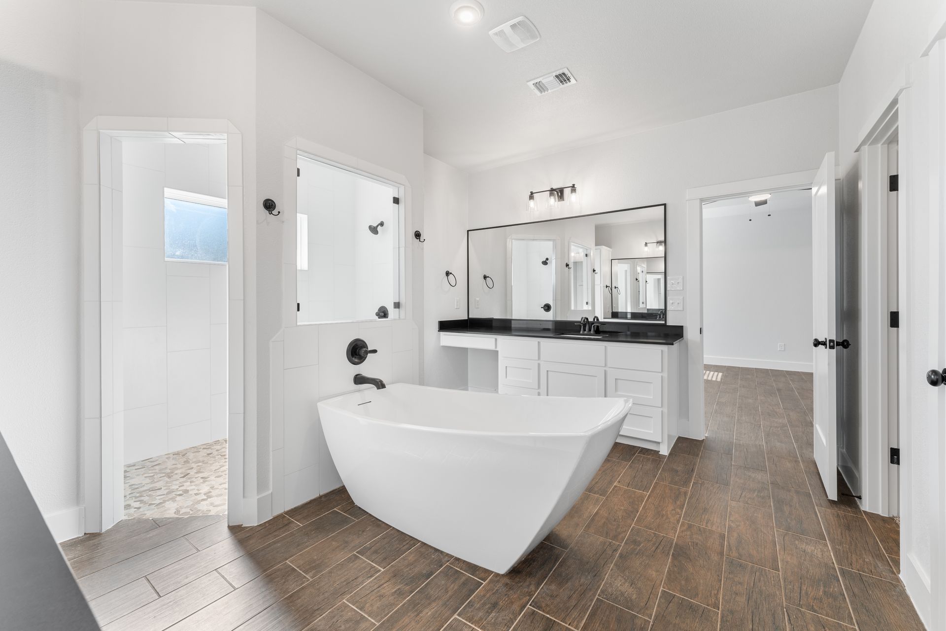 Modern white bathroom with a freestanding tub, vanity, and wood-look tile floor.