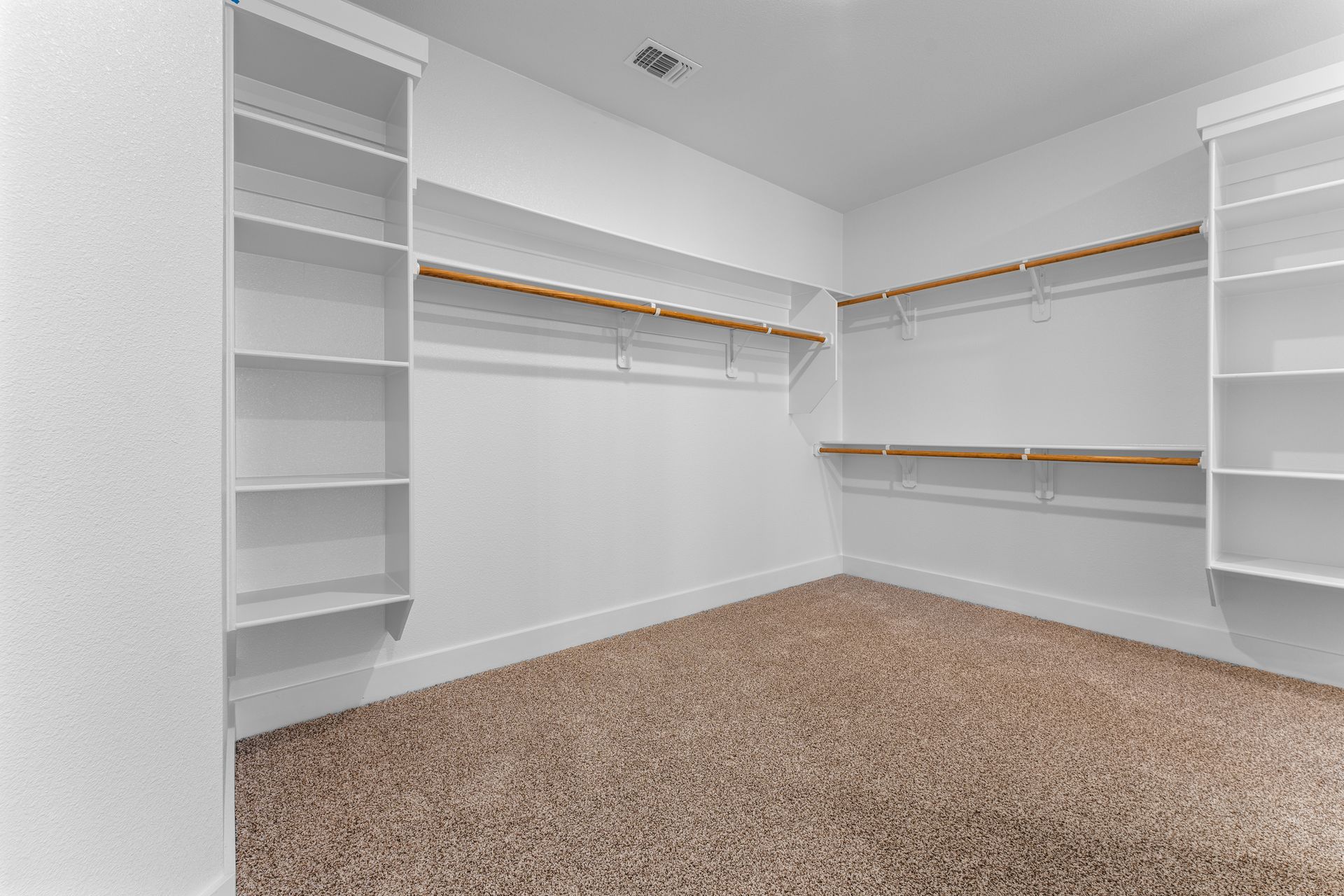 Empty walk-in closet with white shelves, beige carpet, and wooden rods.