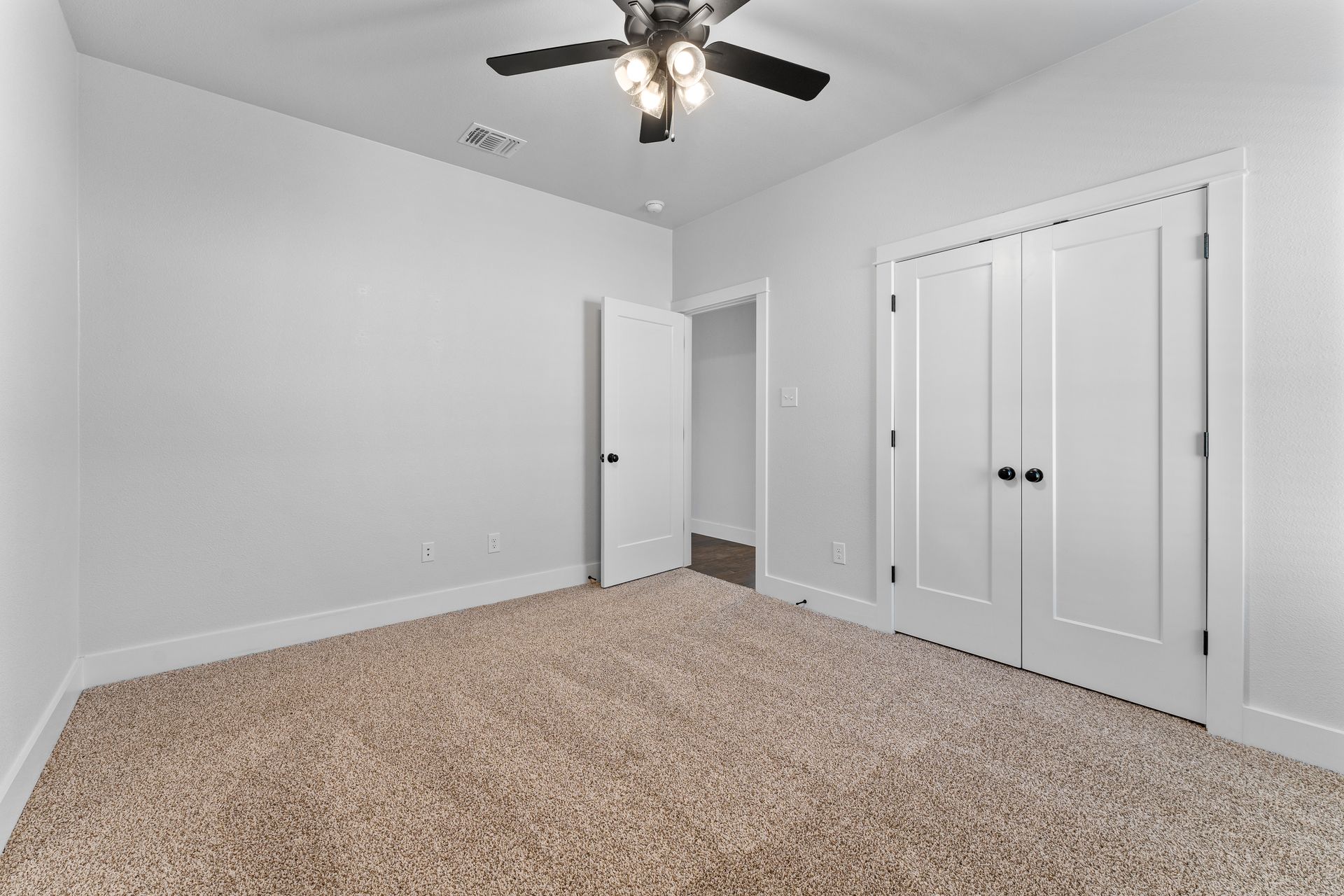 Empty bedroom with beige carpet, white walls, two white doors, and a ceiling fan.