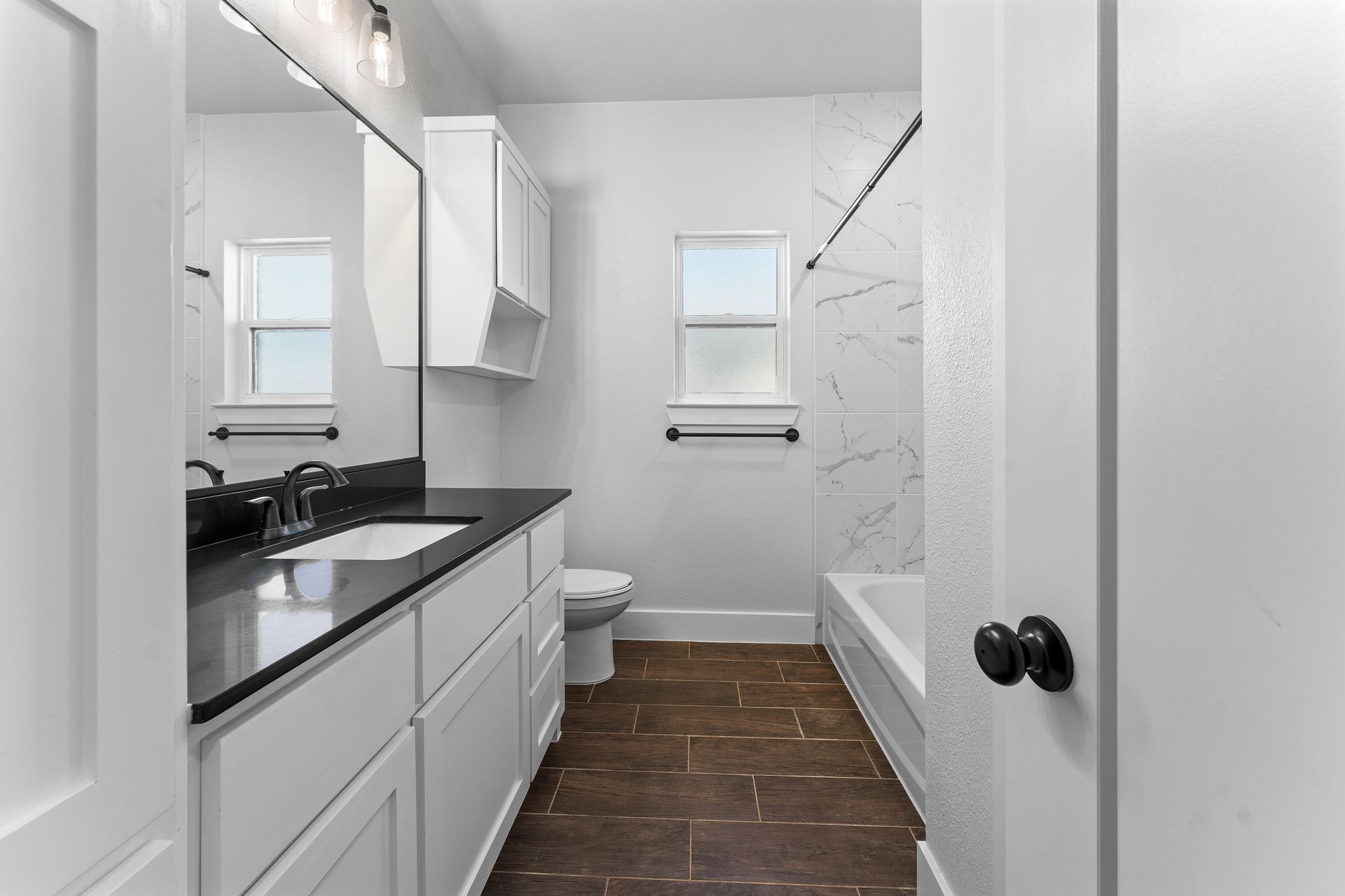 Bathroom with white cabinets, dark countertop, and brown tile floor.