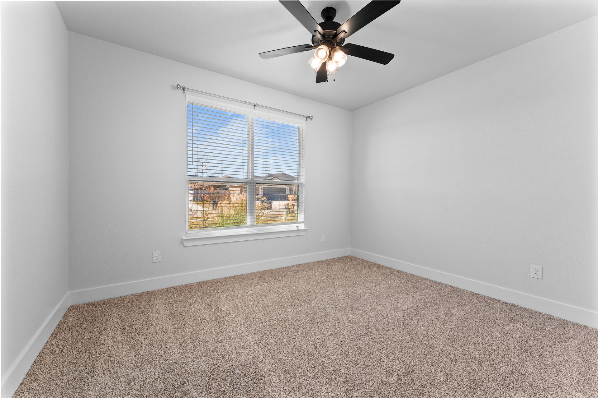 Empty bedroom with beige carpet, a window with blinds, and a ceiling fan.