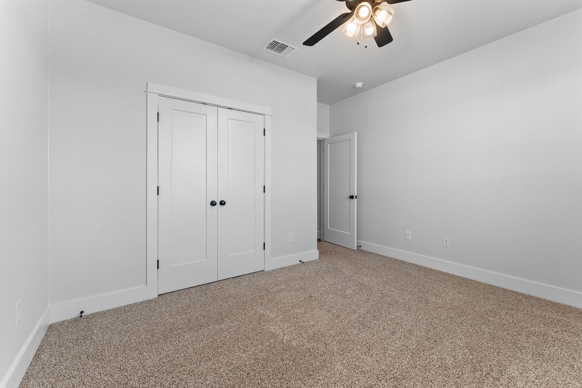 Empty room with white walls, closet, and door, beige carpet, and a ceiling fan.
