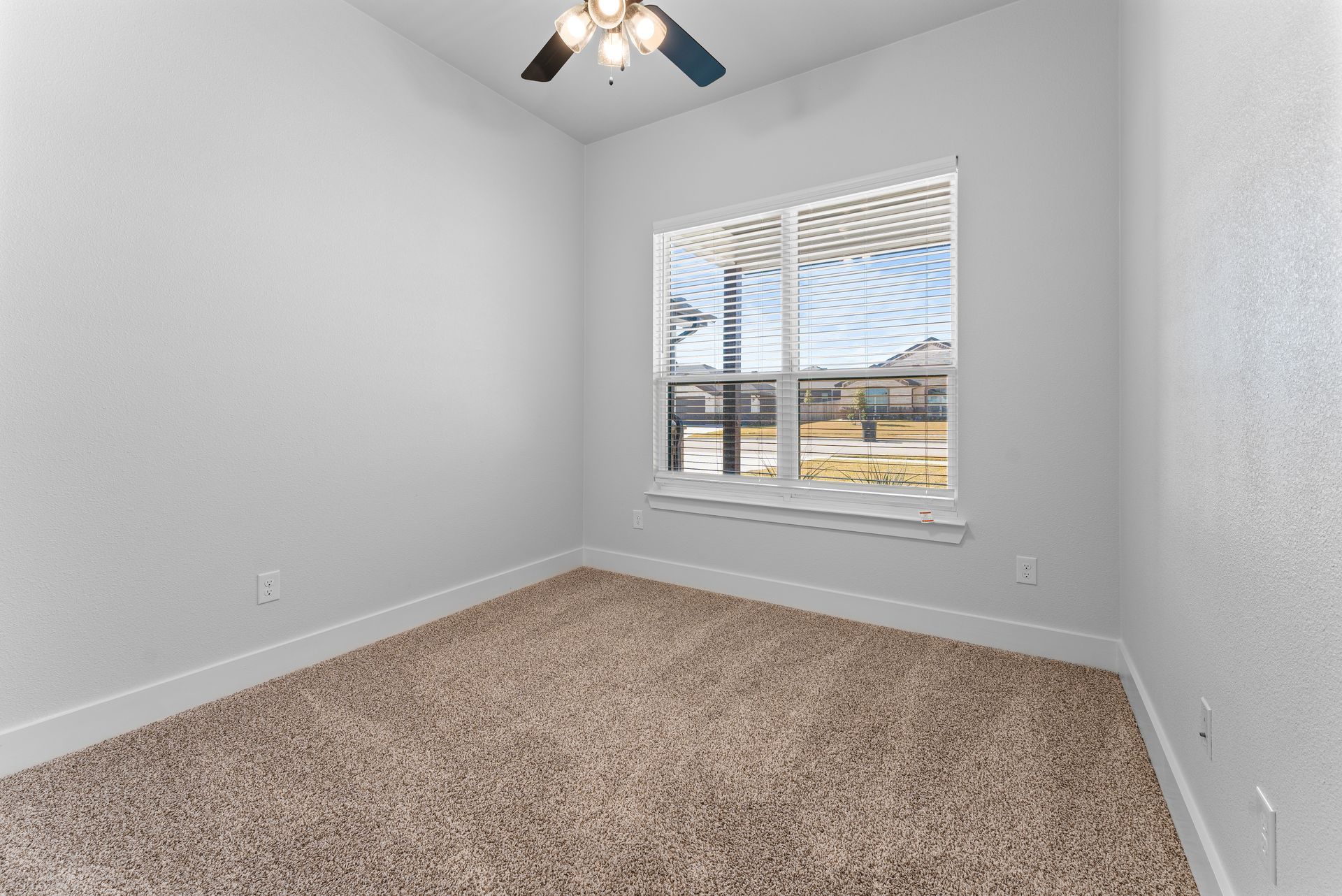 Empty room with beige carpet, white walls, window with outdoor view, ceiling fan.