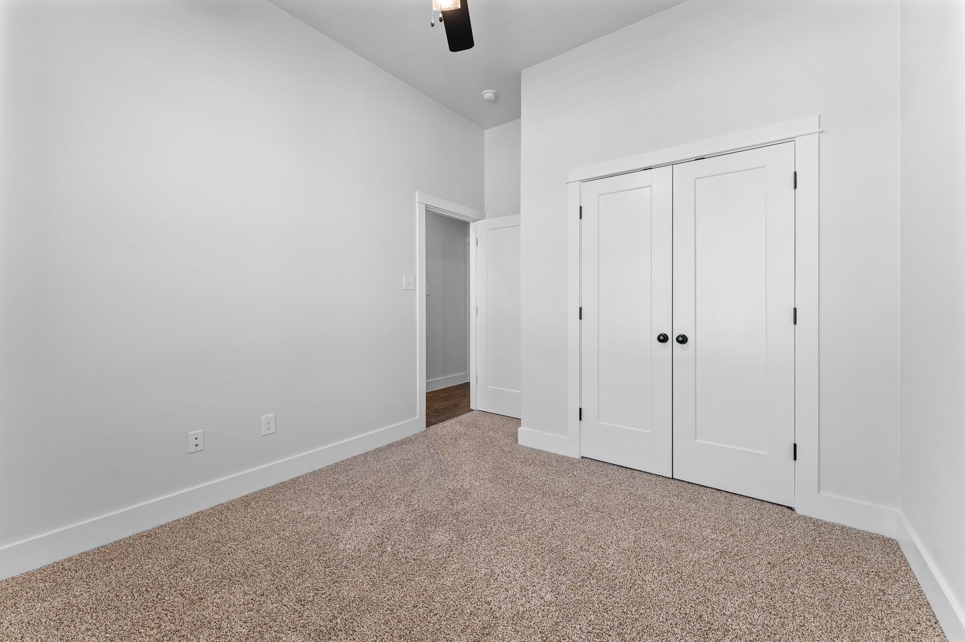 Empty bedroom with white walls, closet, and tan carpet.