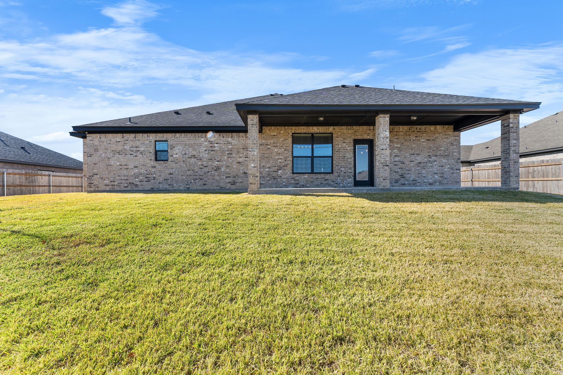 Back view of a brick house with a covered patio and a grassy lawn under a blue sky.