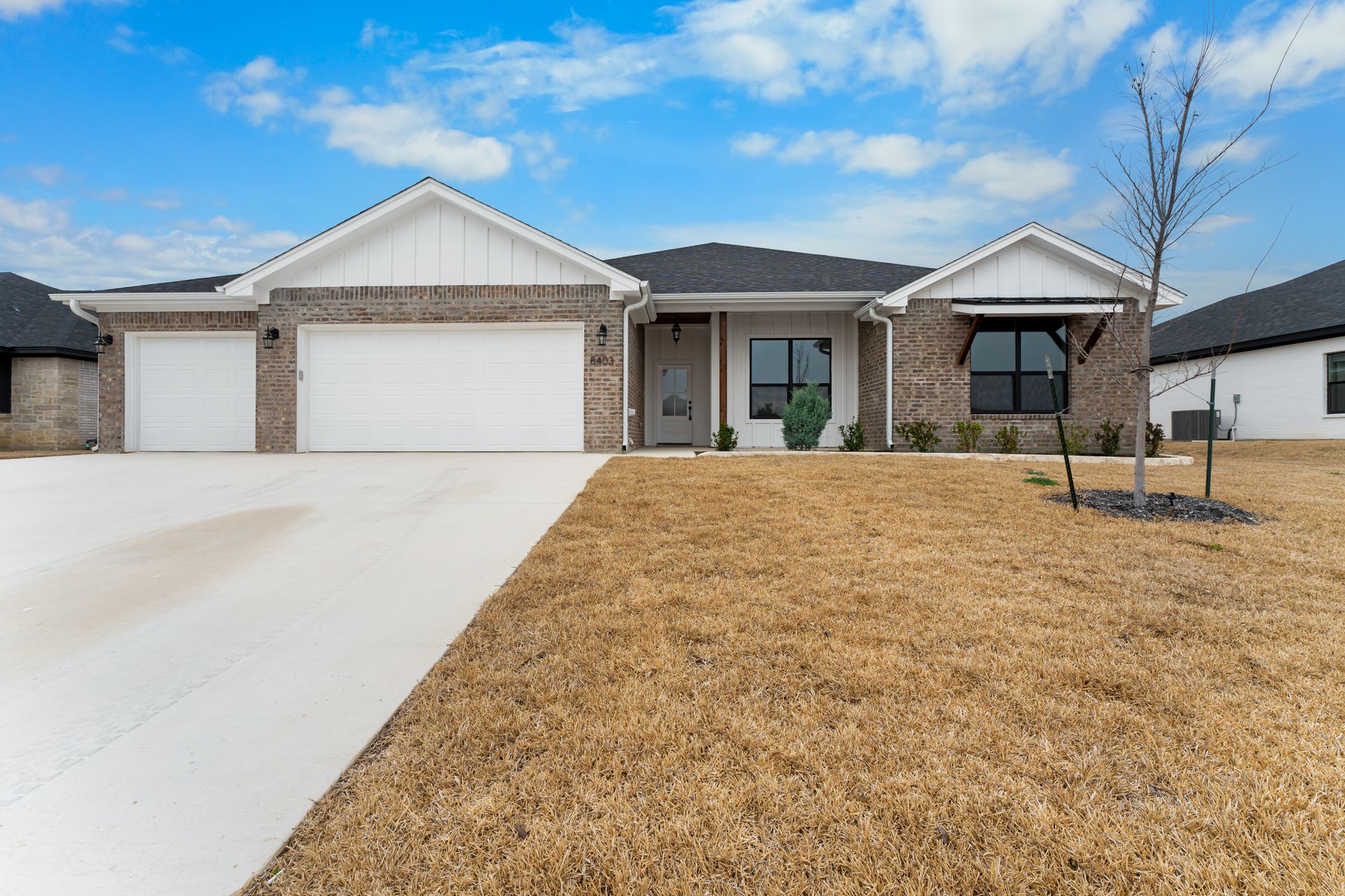 Brick and white house with attached garage and dry brown grass yard.