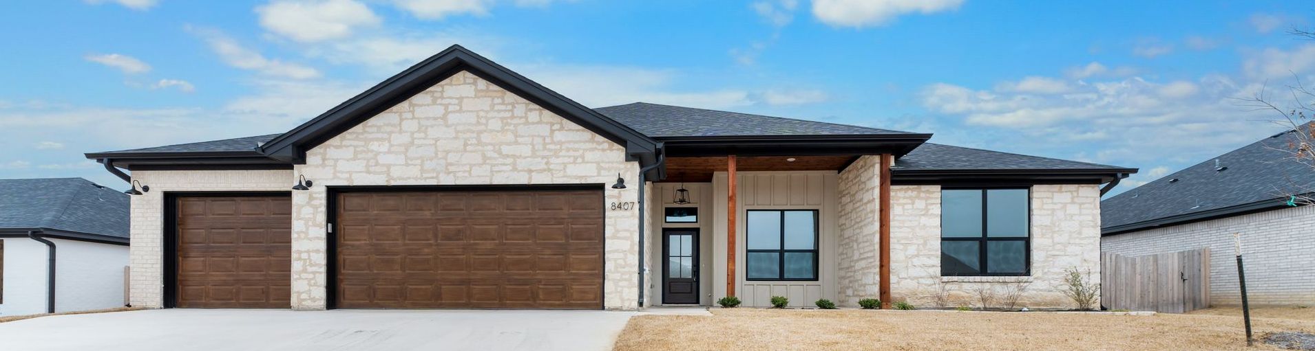 Modern home with stone facade, brown garage doors, and a blue sky.
