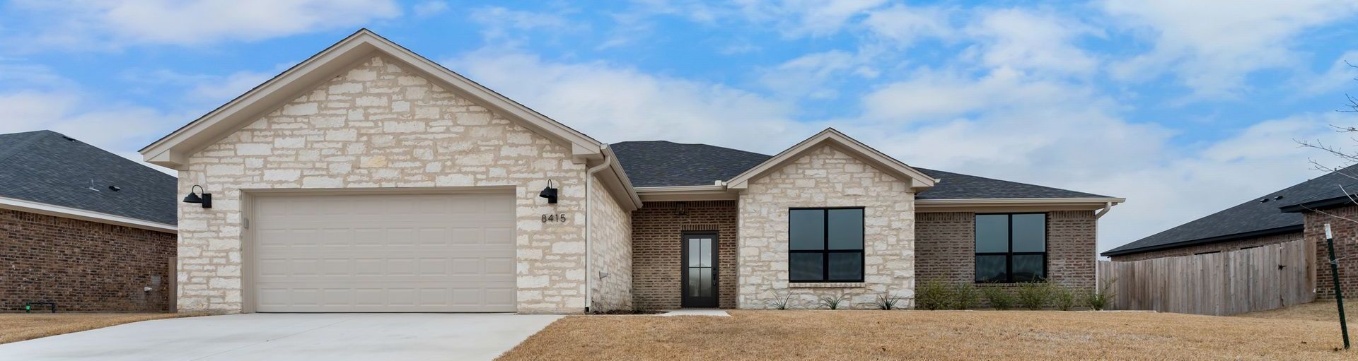 Stone-clad single-family home with a two-car garage under a cloudy blue sky.
