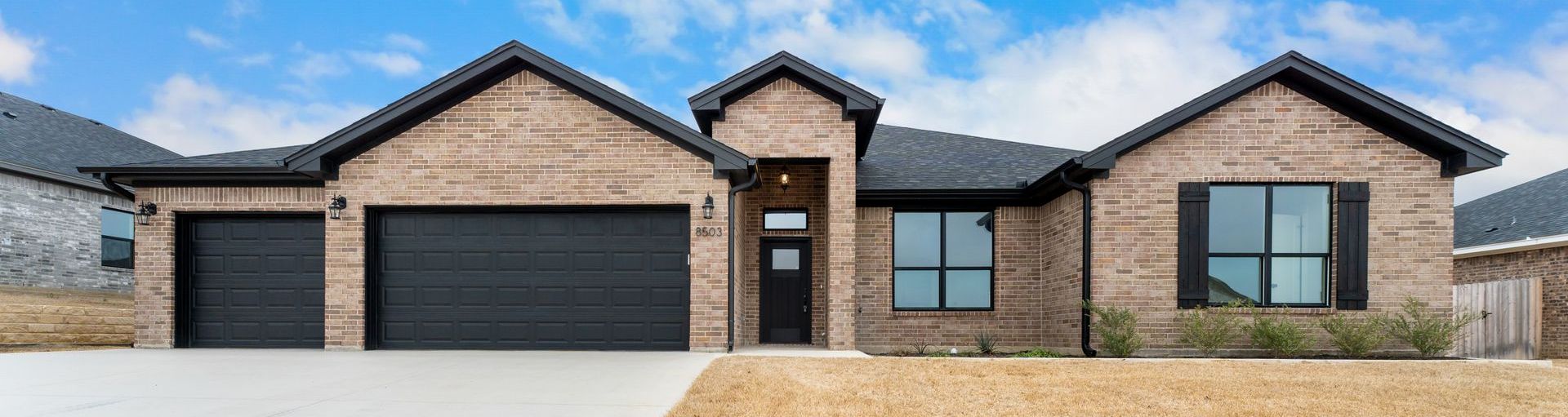 Brick house with black trim, a three-car garage, and a blue sky.