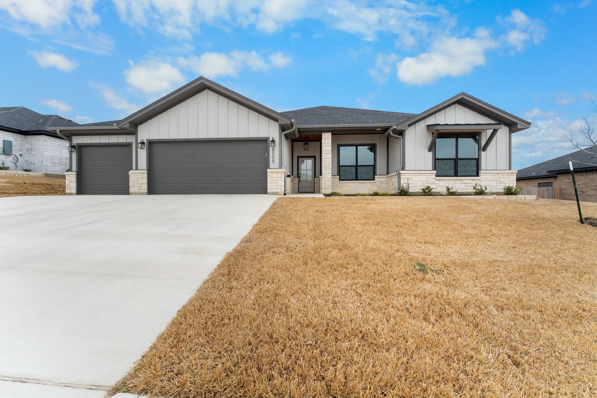 Modern, single-story house with gray siding, two-car garage, and dry, brown grass lawn.
