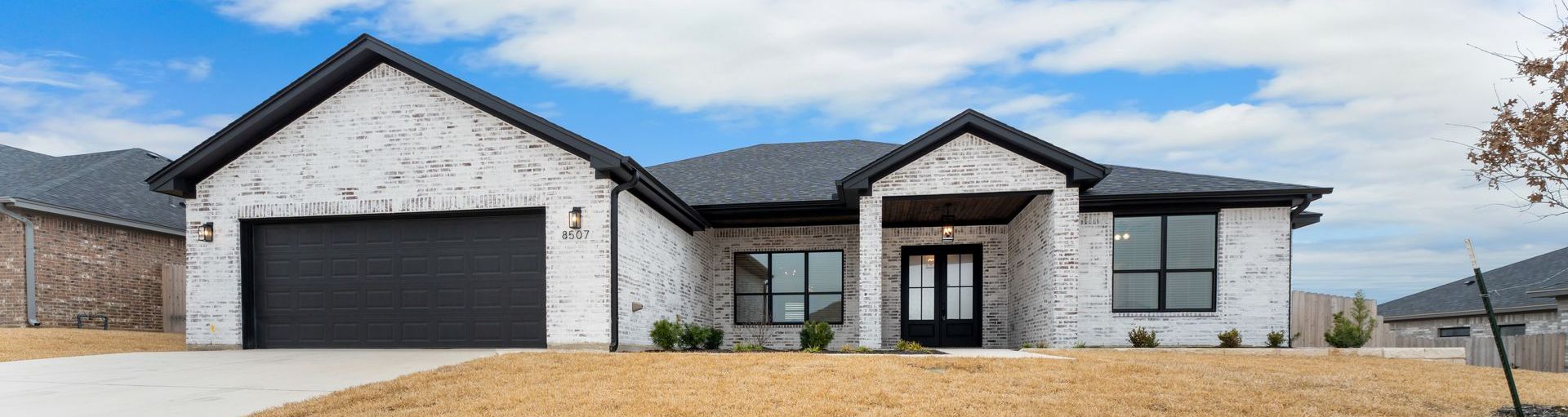 White brick house with black roof and trim, black garage door, and double front doors, under a blue sky.