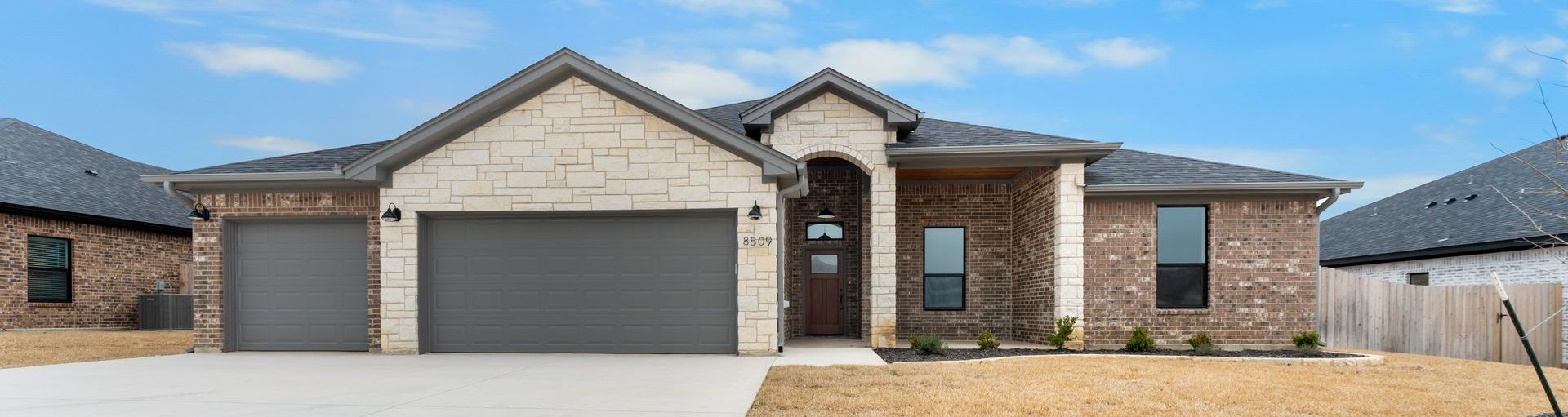 A brick and stone single-story house with a gray garage door under a cloudy sky.