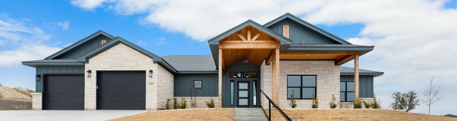 A modern, single-story house with a blue roof, white exterior, black garage doors, and a covered front porch.