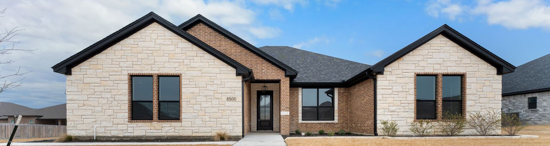 A light-colored stone-faced home with a dark roof and black window frames.