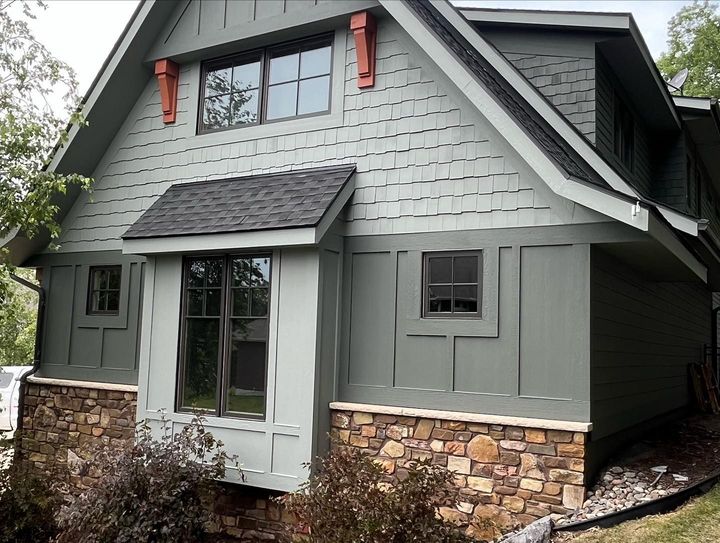 Gray house exterior with stone base, green siding, and a front porch window