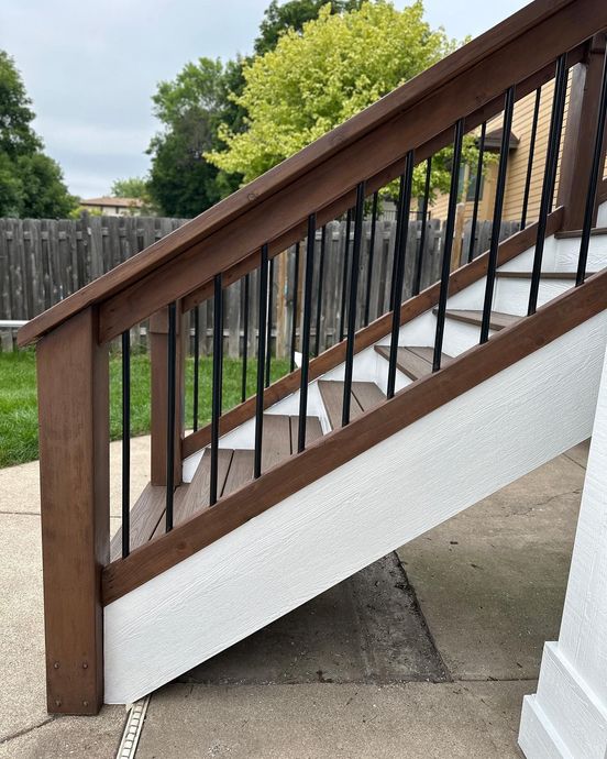 Wooden outdoor stair railing with black balusters and white trim beside a house