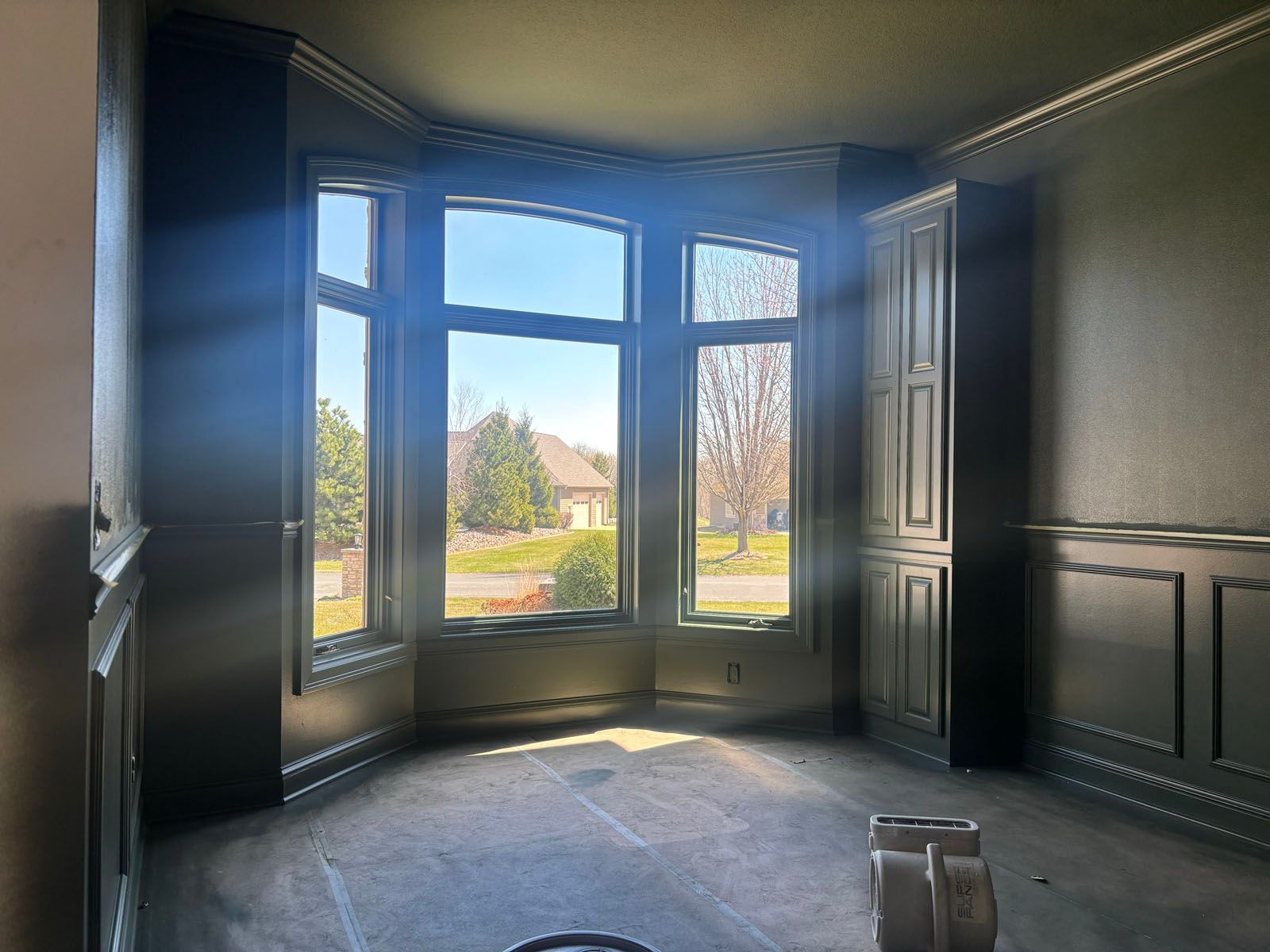 Empty room with bay window, dark wood trim, and sunlight streaming onto the floor.