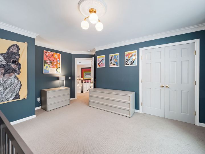 Blue bedroom with white closet doors, dressers, framed art, and a ceiling light.