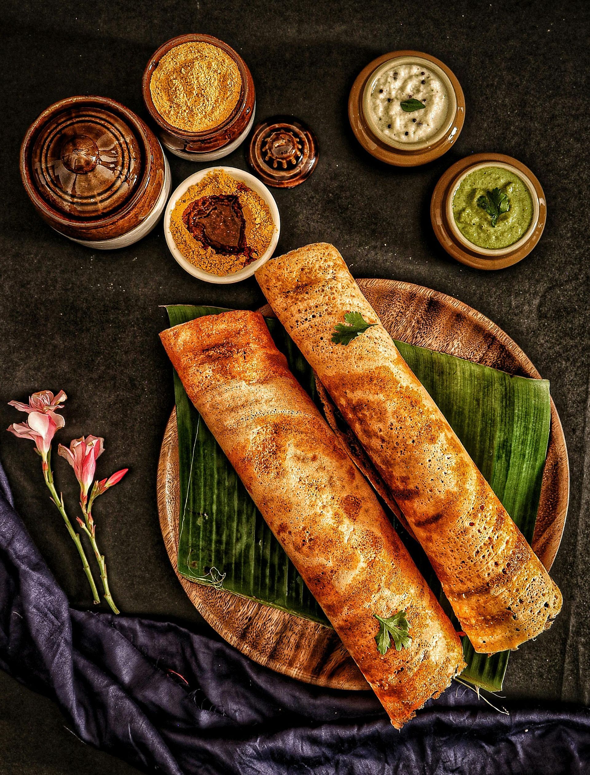 “Crispy masala dosas served with chutneys and sambar on a banana leaf platter at a south indian restaurant.”