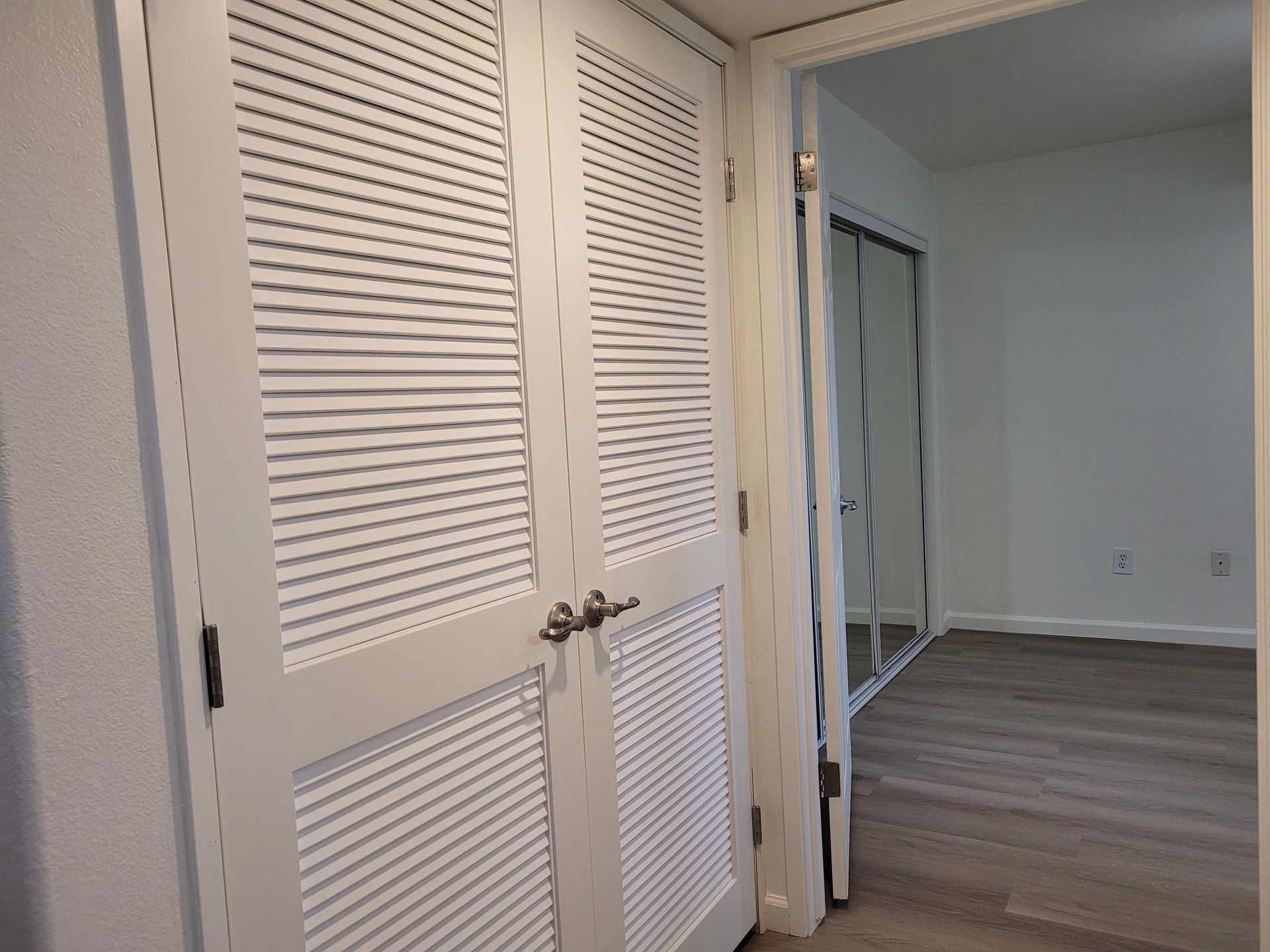 A closet with shutters on the doors is open to a bedroom.