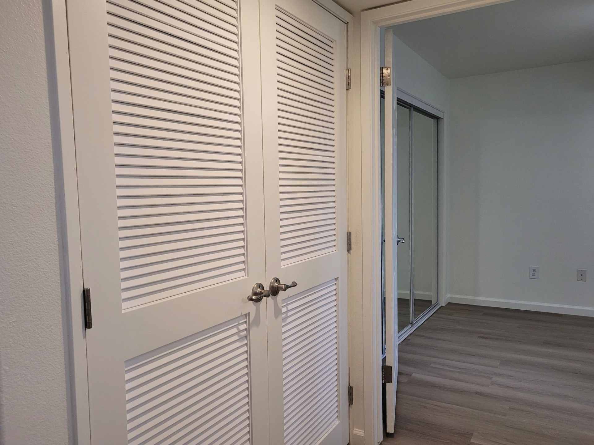 A closet with shutters on the doors is open to a bedroom.