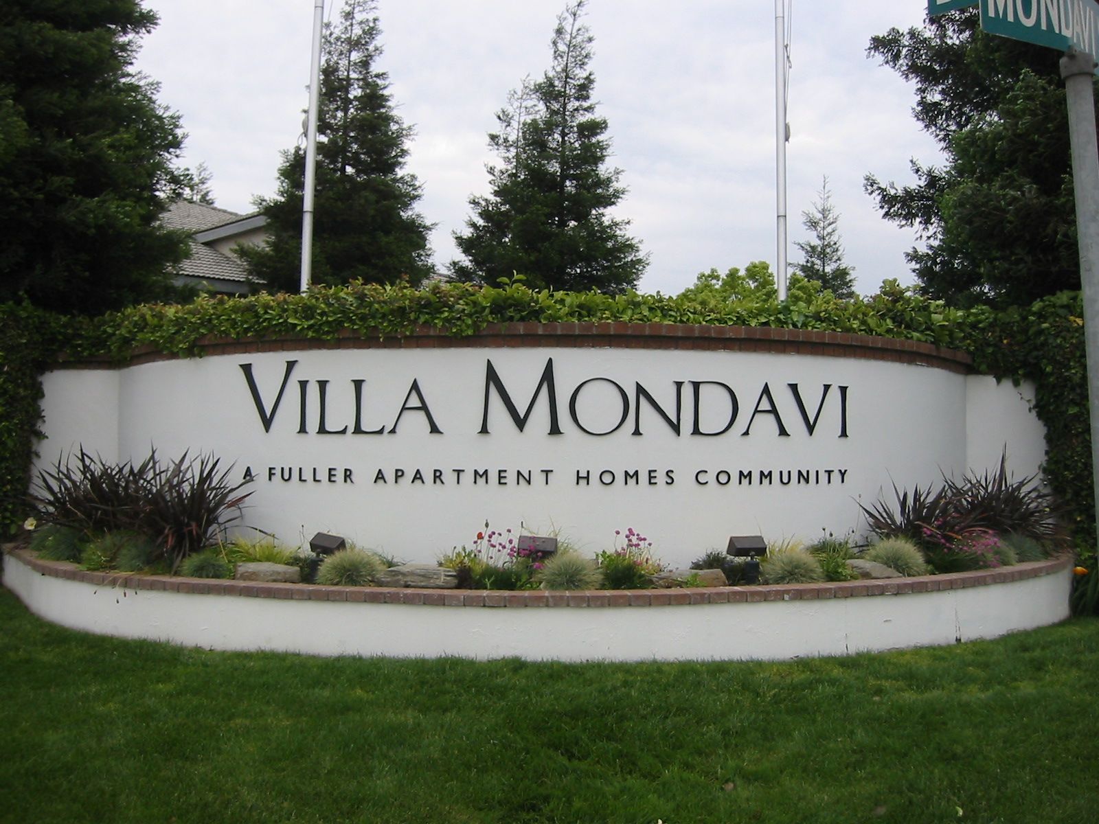 A sign for villa mondavi is surrounded by grass and trees