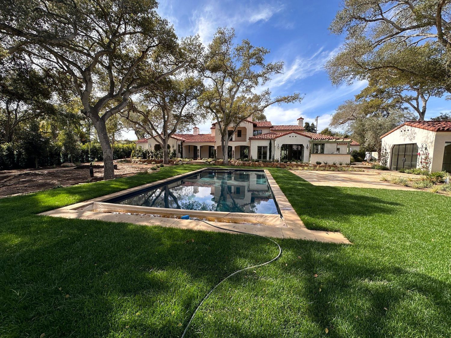 Suburban house with a white garage, brown shingle roof, and front porch in a landscaped yard