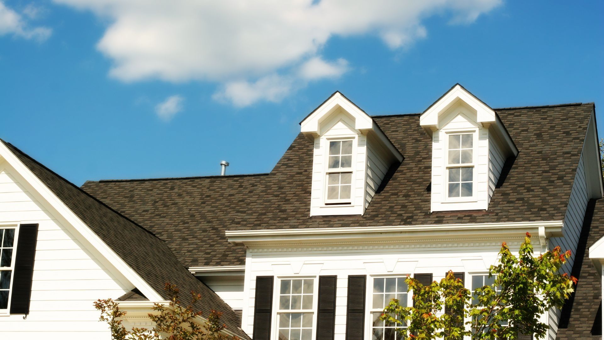 White farmhouse with gray roof and black garage doors.