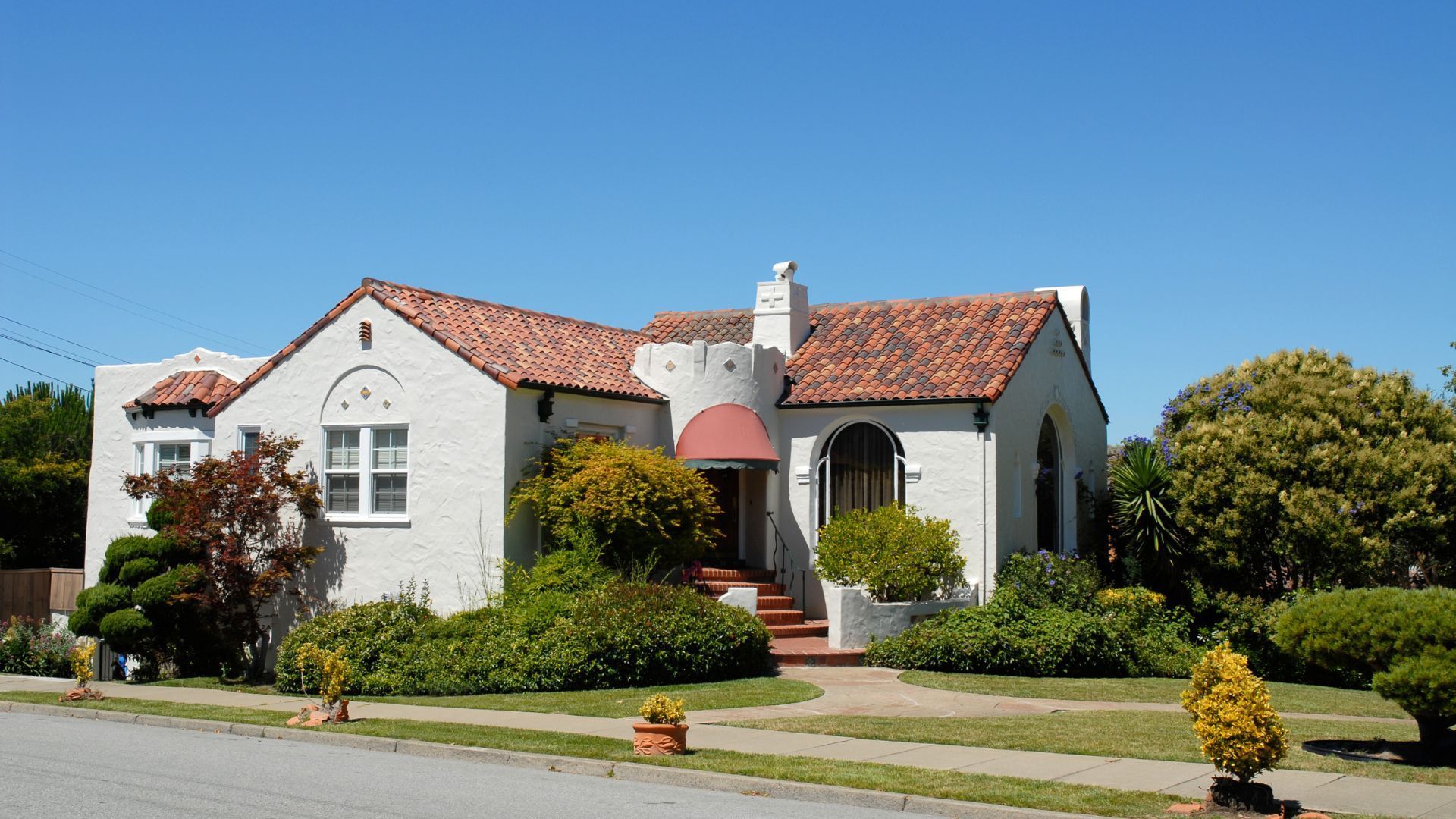Two-story beige house with attached garage, driveway, and landscaping under a sunny sky.