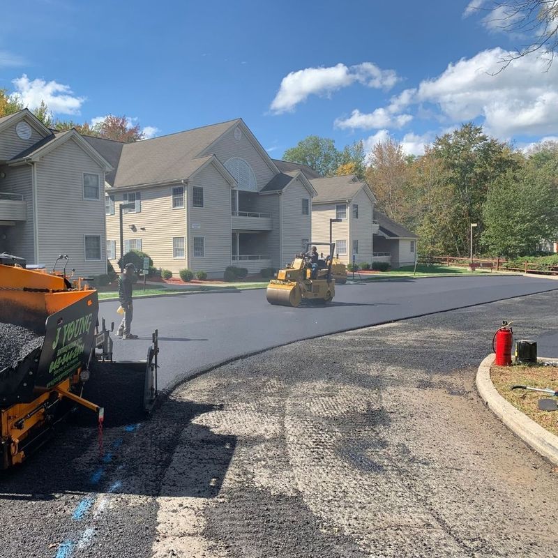 Asphalt paving in progress at apartment complex with machinery and worker.