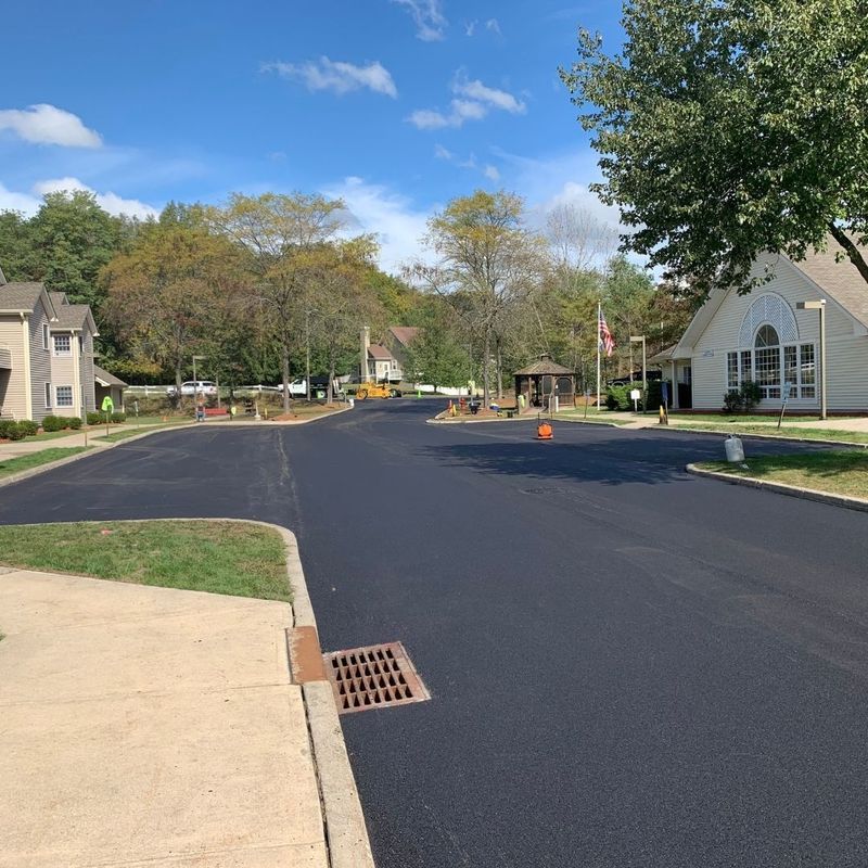 Newly paved black asphalt road with buildings and trees under a blue sky.